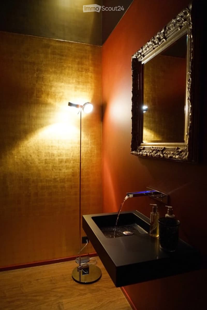 a bathroom with red walls, a golden-textured wall, a mirror, a sink, and a lamp