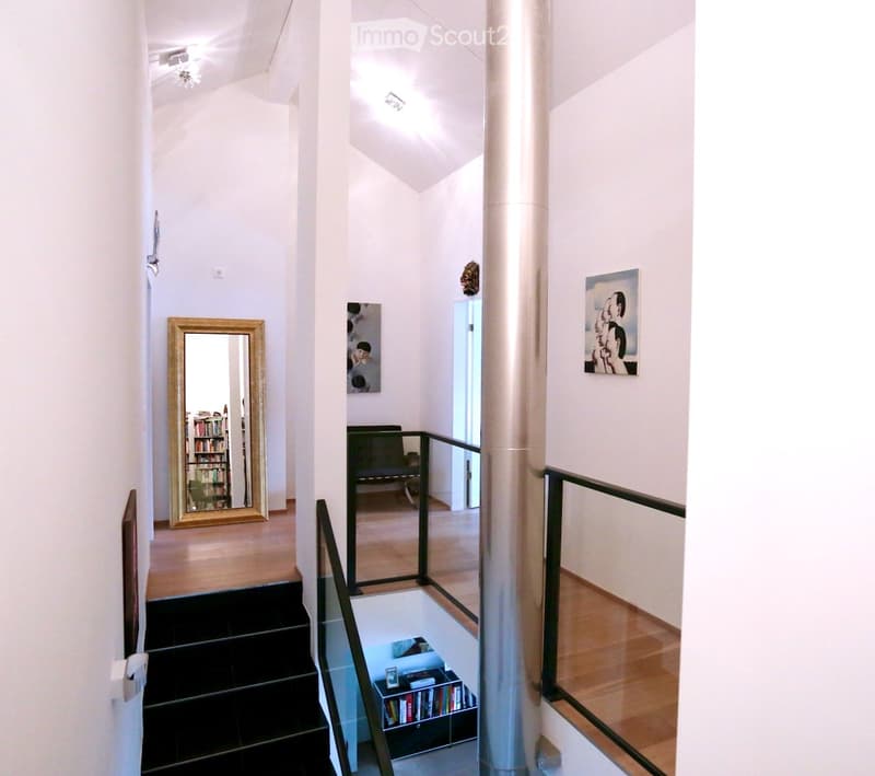 White walls, wooden floor, mirror, gallery railing, paintings, staircase