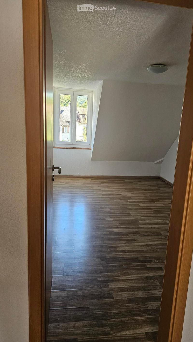 Empty room with wooden floors and white walls. There is a window and a ceiling light.