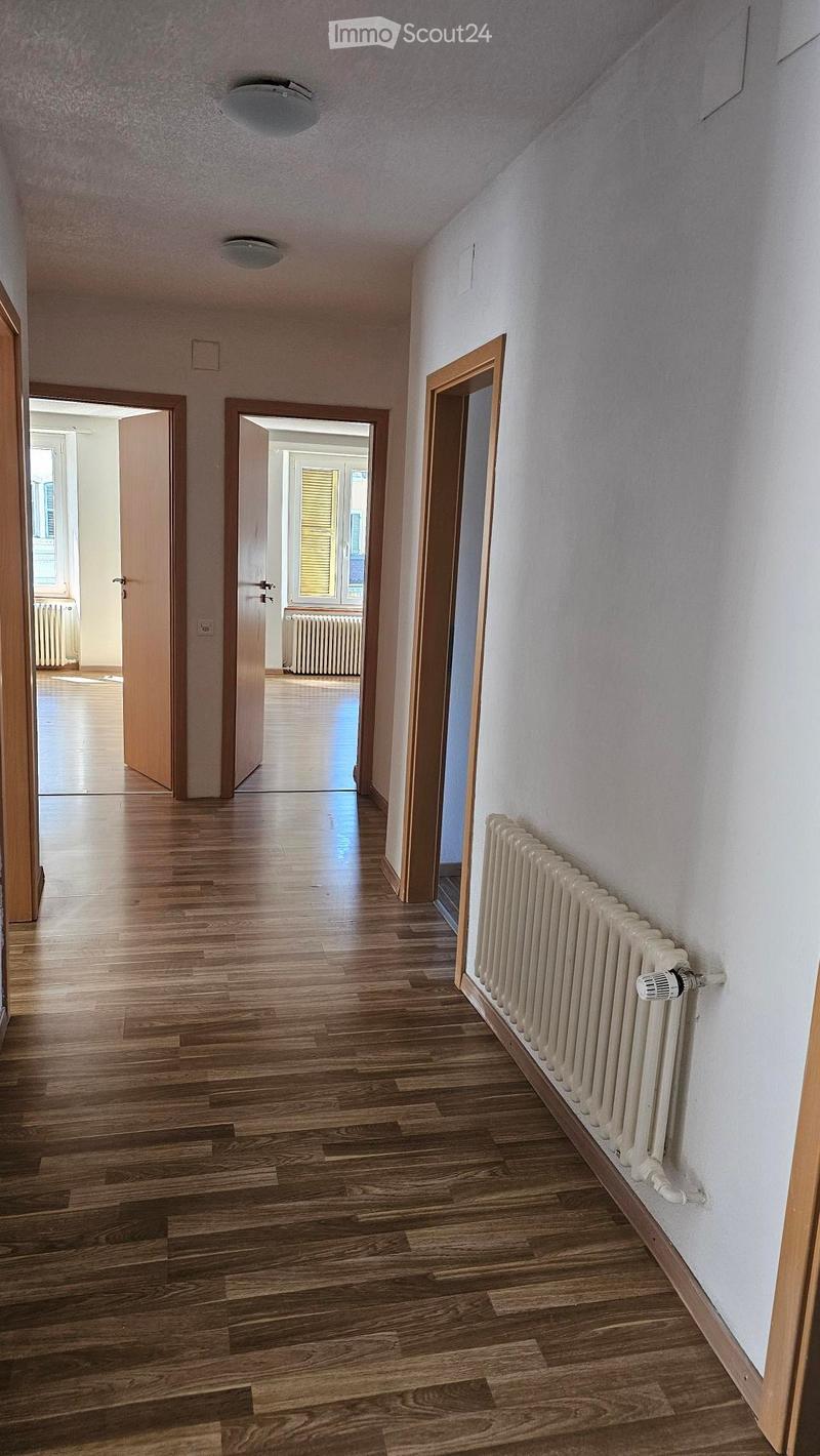 Hardwood floor, white walls, 3 open doors, radiators, open rooms with windows.