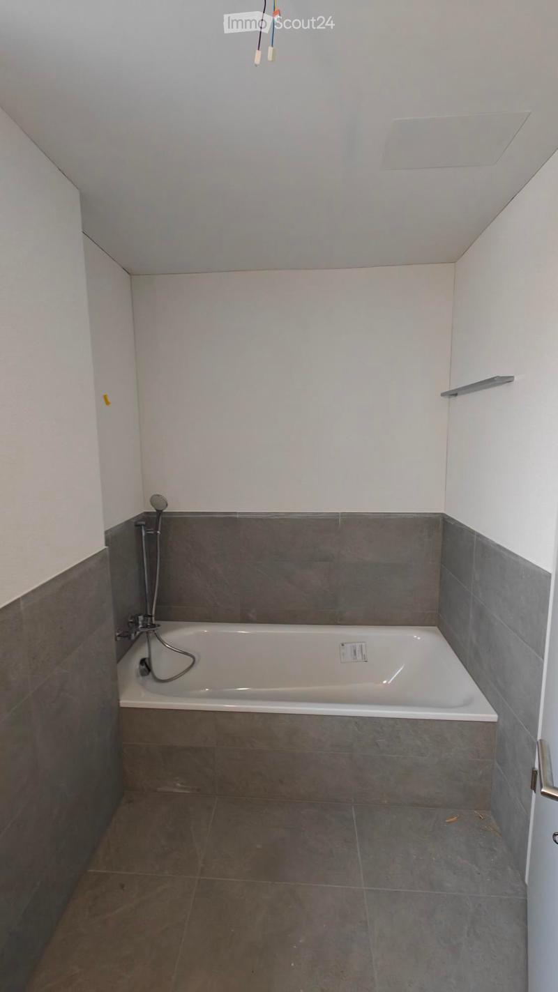 Bathroom with a bathtub, gray tiled floor and walls, shower head attached to wall, no furniture
