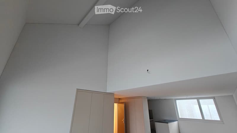 Empty room with white walls, ceiling, and floor. There is a large wardrobe and a small cabinet. There is a window with blinds.