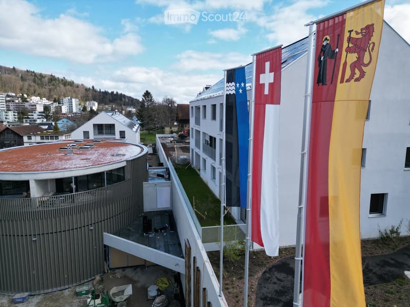 Modern building with glass windows, red roof, flags, and a circular structure nearby