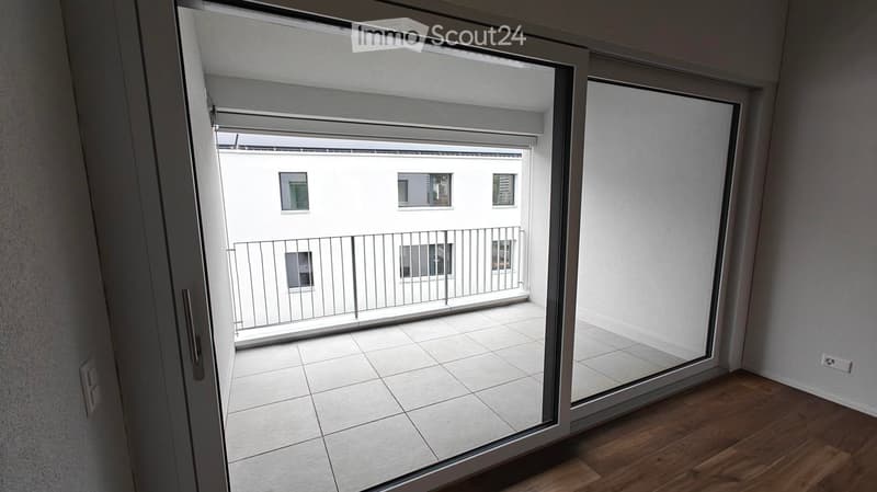 Open sliding glass door leads to a tiled balcony with a metal railing, overlooking a neighboring building.