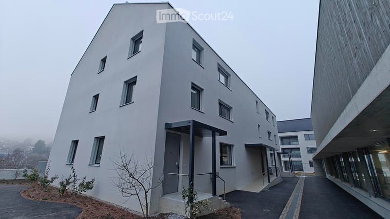 Modern apartment building with white exterior walls, large windows, black canopy, grey driveway