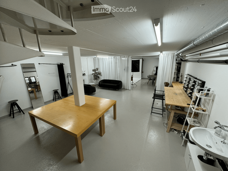 Wide open room with white walls, wooden tables, benches, couch, mirror, plants, ceiling lamps