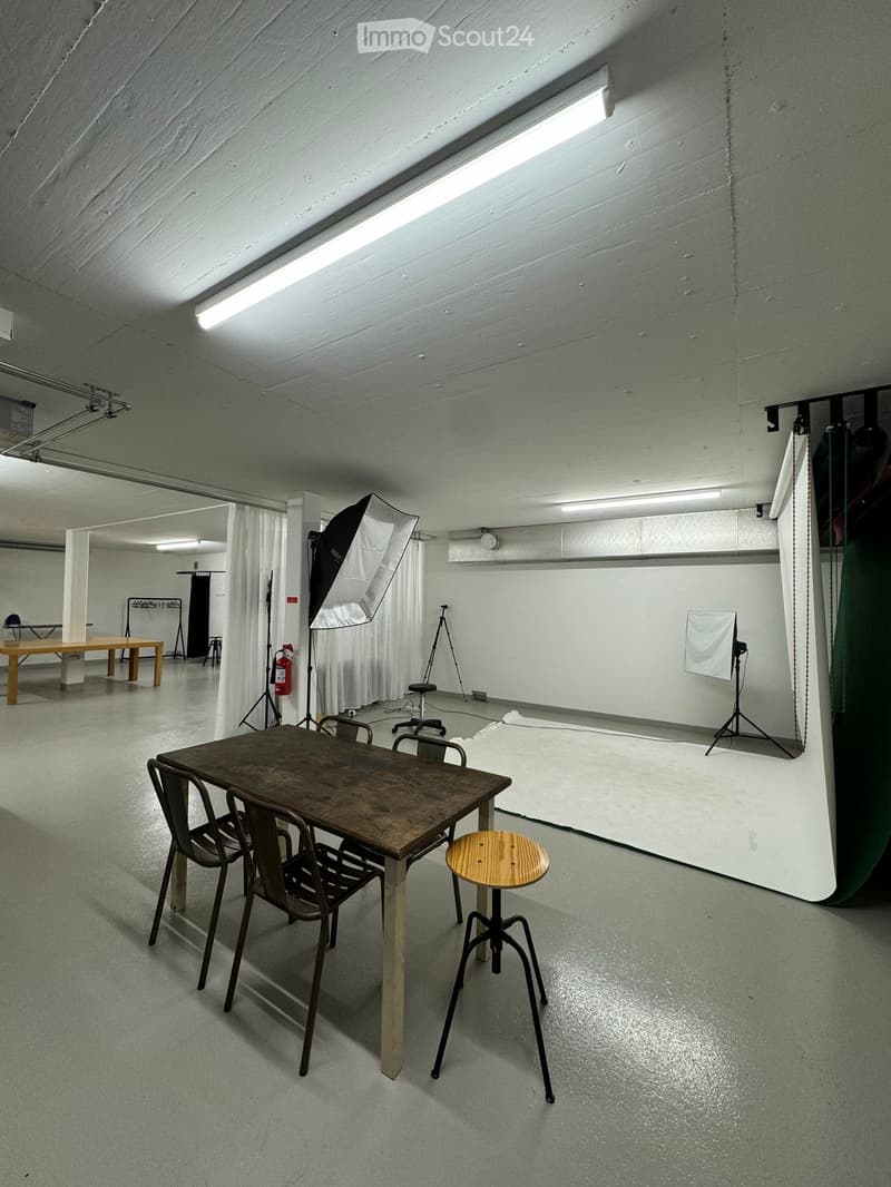 photography studio, wooden table and chairs, white floor, white walls, large white backdrop, lighting equipment