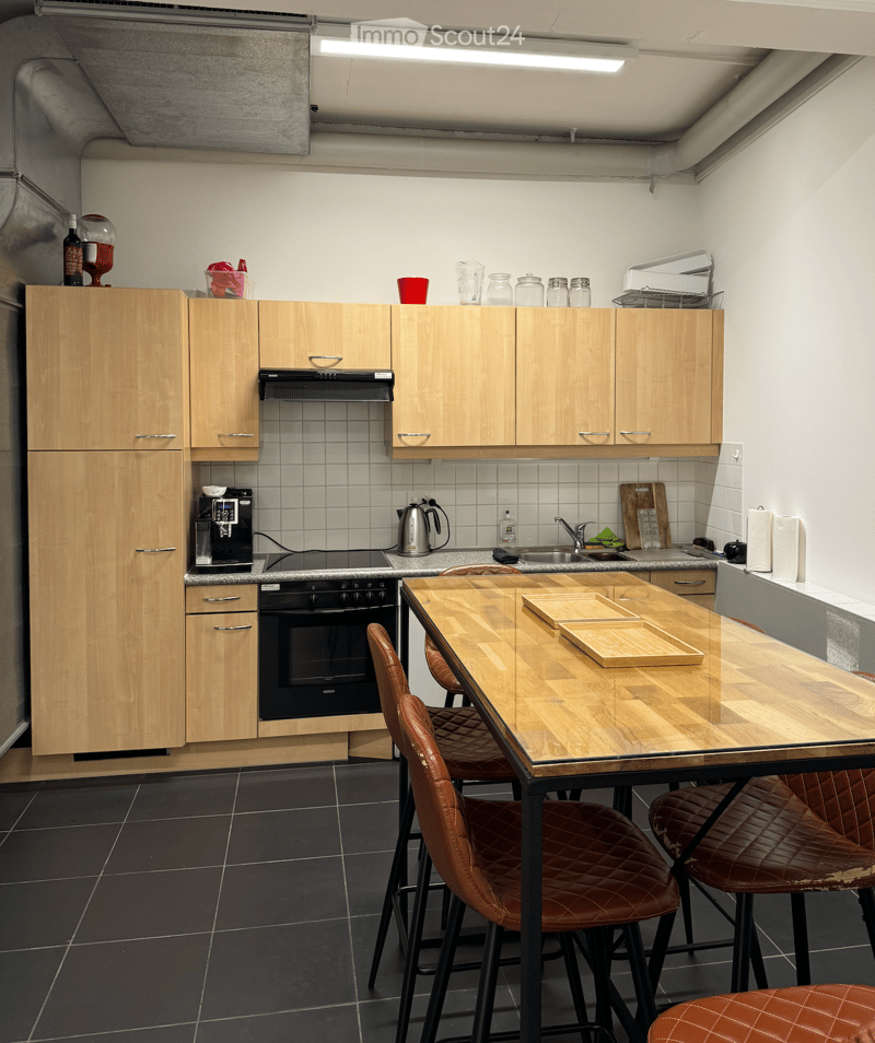 wood cabinets, black oven, brown chairs, wooden table, sink, refrigerator, countertop, lamps, electrical appliances, bottles, wine glass, jar, kettle, chopping board, roll of paper towels, sink faucet, coffee machine