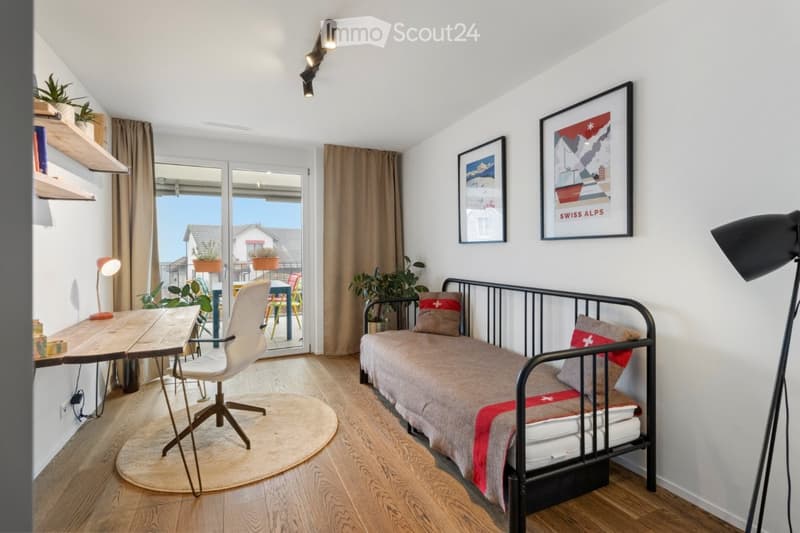 modern bedroom with wooden flooring, daylight lamp, single bed, armchair, desk, plant, curtains, framed pictures, and an outdoor view