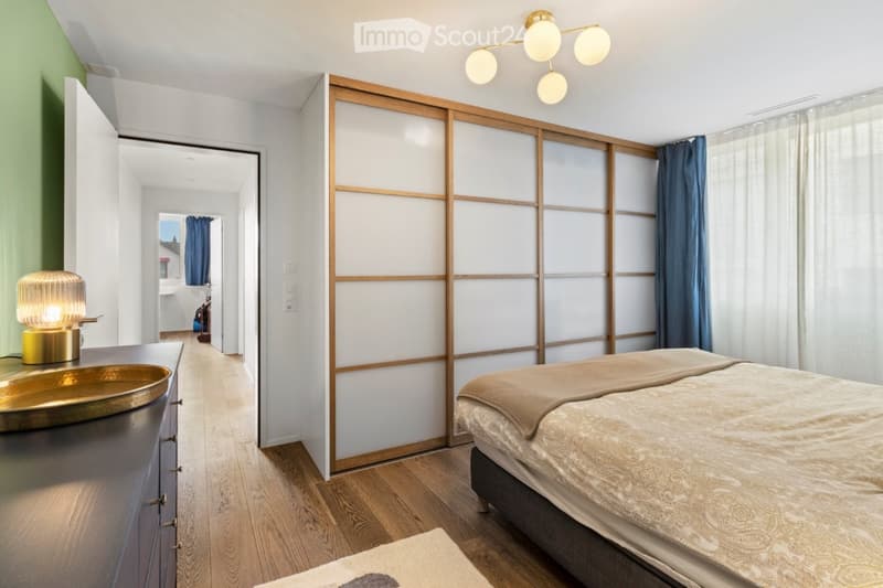 bedroom with bed, wooden floor, nightstand with lamp, sliding door, carpet, blue curtains, large window