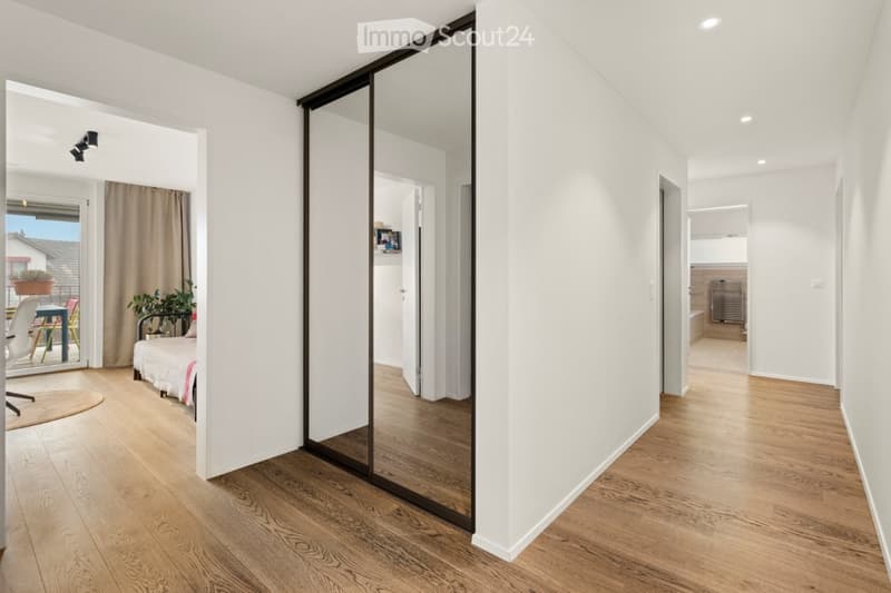 Spacious room with a sliding mirror door, wooden floor, white walls, bed with a single bed, small rug and a bedsheet, a patio with a table and chairs visible from the glass door, and a potted plant.