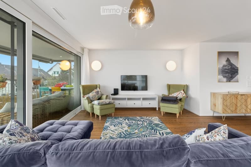 Glass doors leading to a terrace, modern minimalist design, white walls, beige wooden floor, comfortable gray sofa, white entertainment unit, flat screen TV, and two green chairs