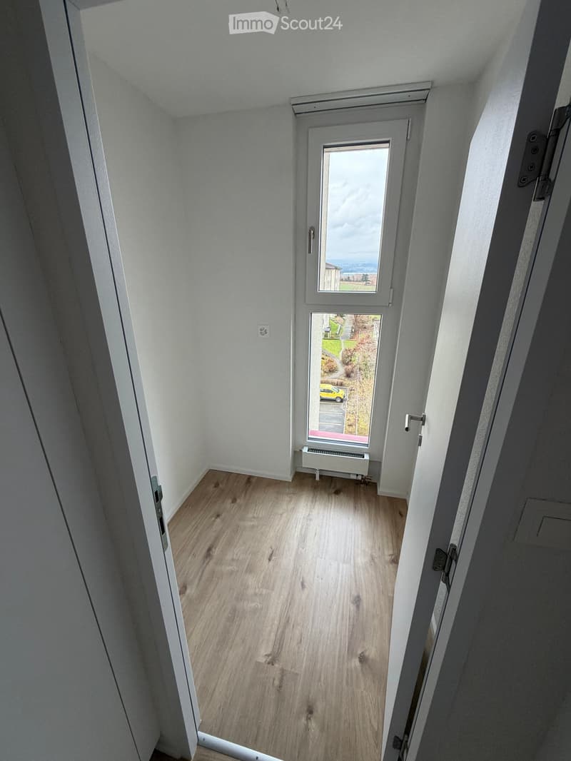 empty room with wooden floor, white walls, window with exterior view, door