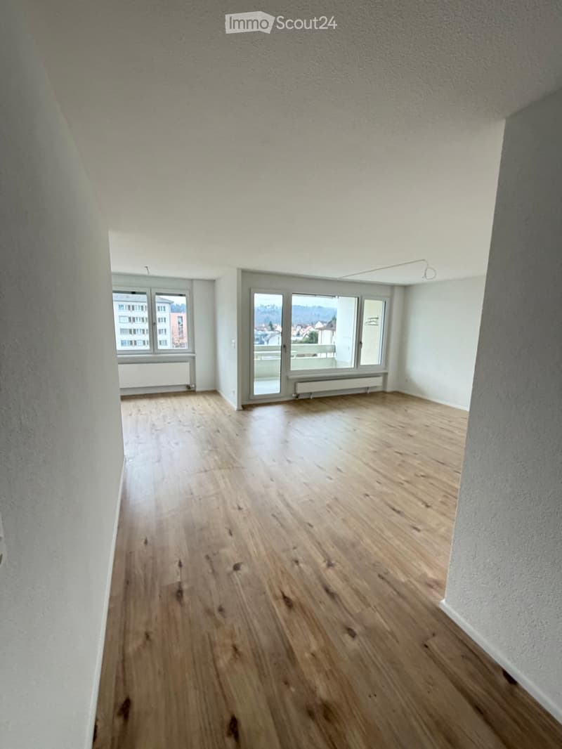 Empty room, hardwood floors, sliding glass doors leading to balcony, windows, white walls
