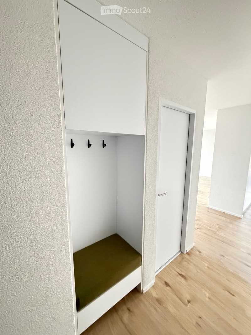 an empty room with wooden floor, white walls, a built-in closet, and a bench