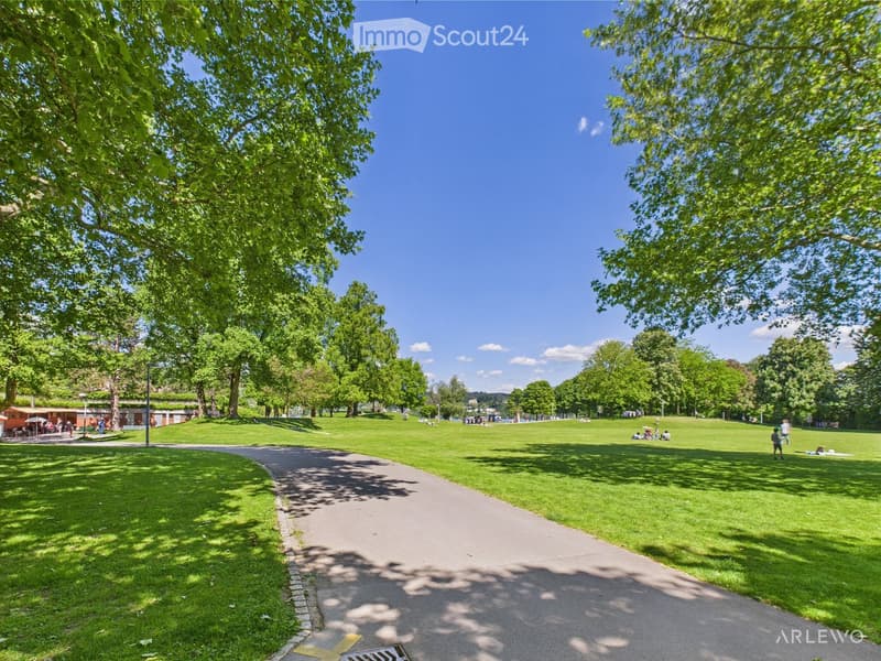 Well-manicured park with several walking paths, trees, green grass and people relaxing