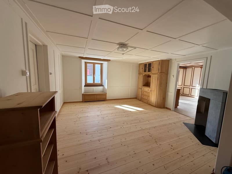 Large room with wooden flooring and white walls, large window, built-in bench, wooden wardrobes, fireplace, wooden shelf