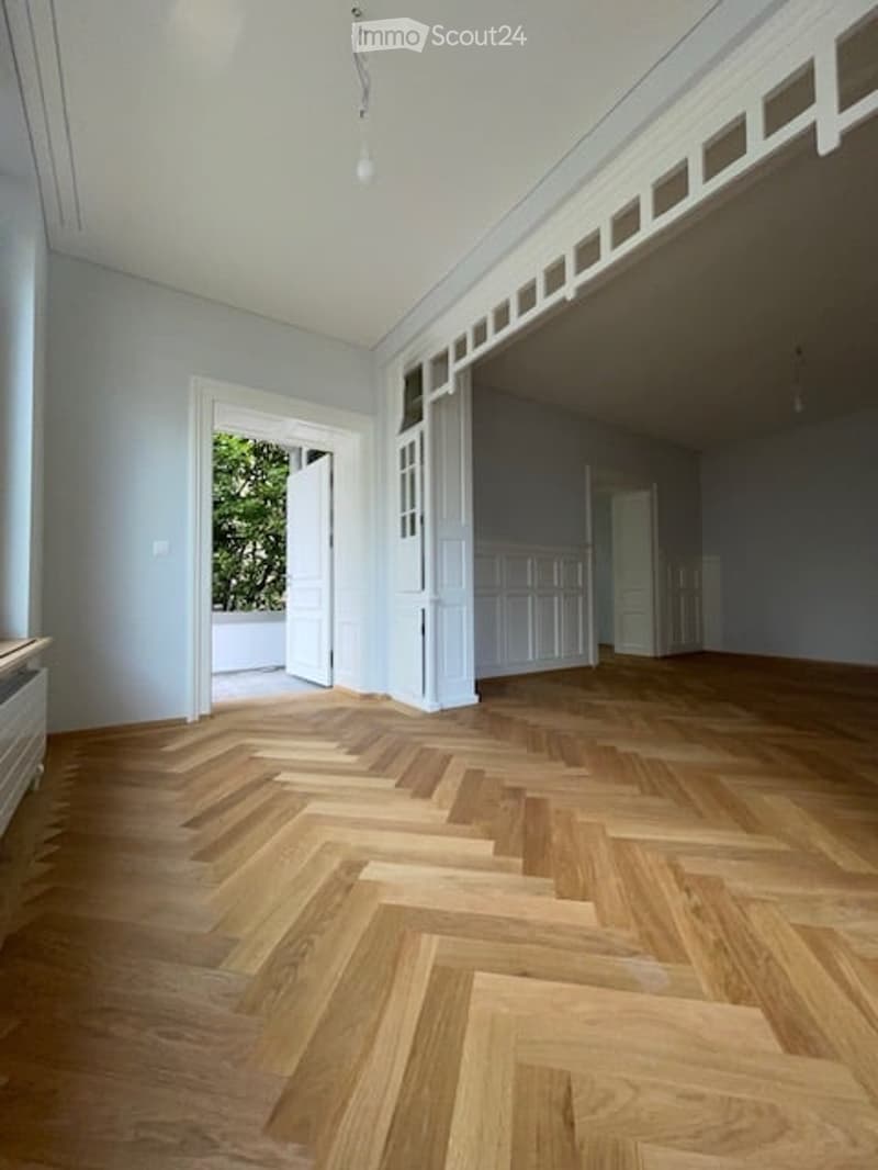 Empty room with wooden parquet flooring, white walls, white doors, and a ceiling with white trim and a hanging light fixture.