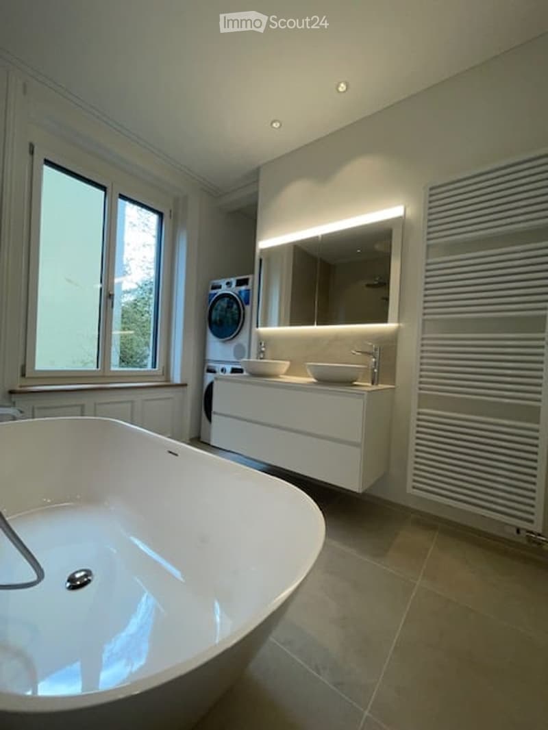 modern bathroom with bathtub, double sink, mirror, washing machine, and window