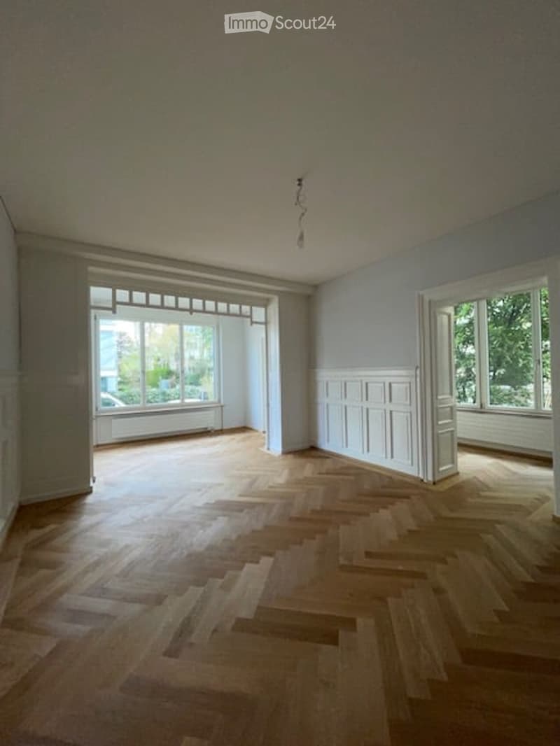 Empty room with wooden parquet flooring, white walls, large windows, and a white ceiling.