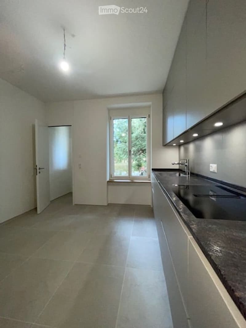 Empty kitchen with white walls, tiled floor, double sink, window, and a door