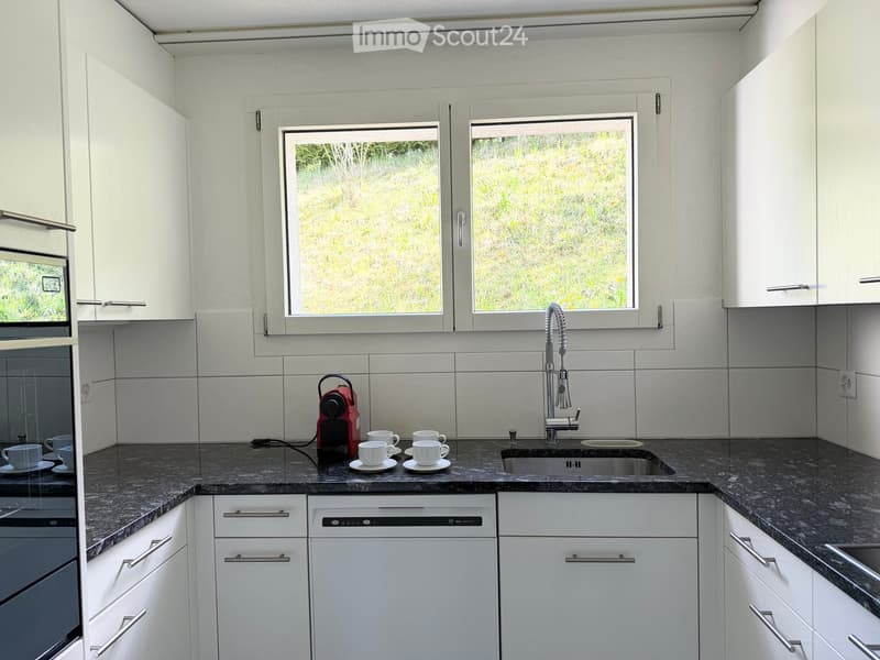 Modern kitchen with white cabinets, granite countertops, stainless steel sink, and a coffee maker on the counter.