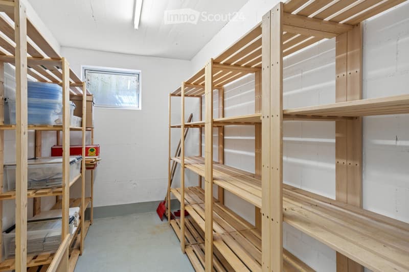 A storage room with multiple wooden shelves filled with storage bins and a broom on the floor.