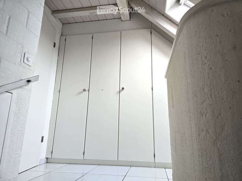 A corner room with white tiled floor, wooden beams on the ceiling and tall white built-in wardrobes