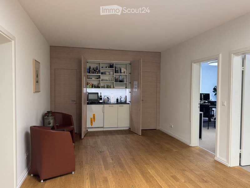 open space with hardwood floors, open kitchen, microwave, coffee maker, open cabinets, picture frame, two brown chairs