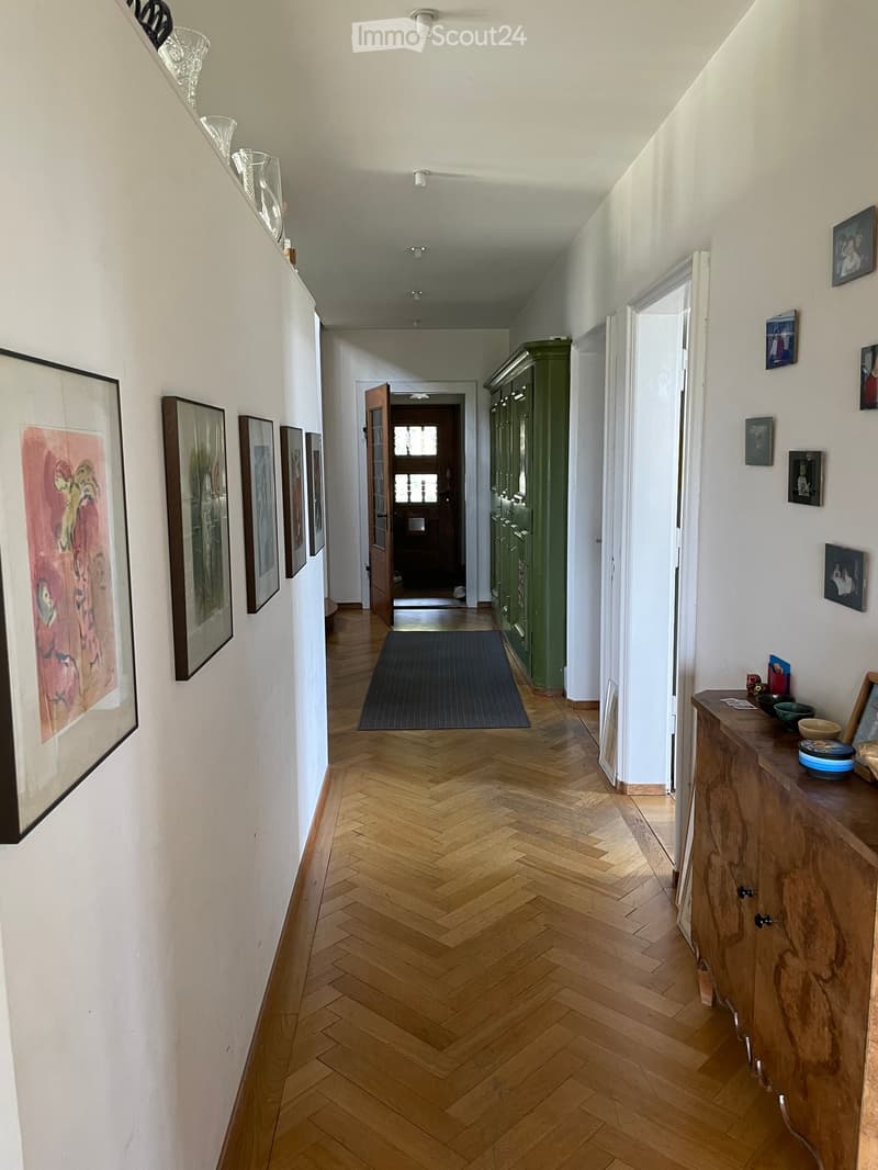 Empty corridor with wooden flooring, white walls, framed pictures, wooden cabinet, a wooden floor rug