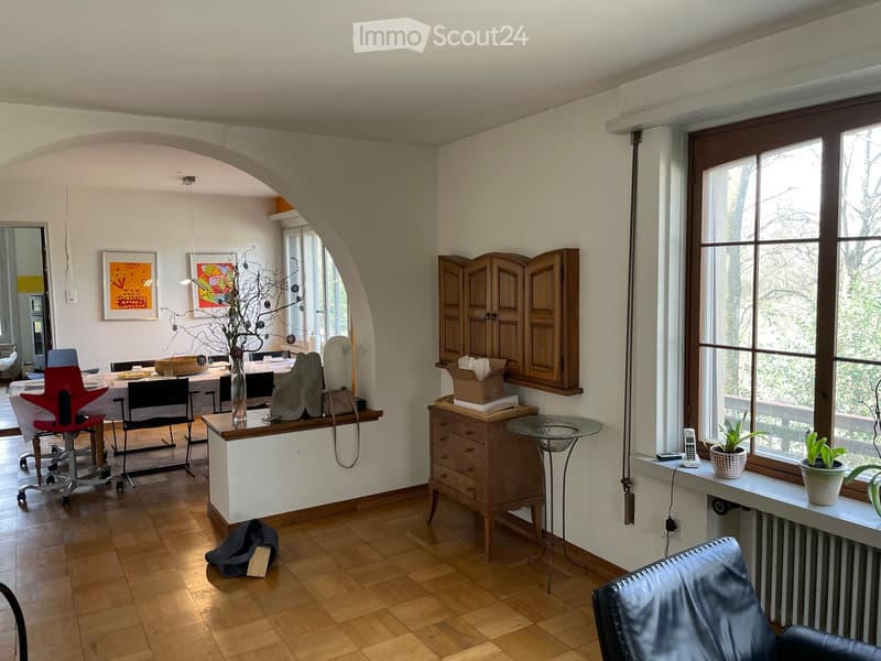 Wooden floor, white walls, arch doorway, dining table with chairs, sideboard, wooden cabinet, round glass table, large window, plants, chair