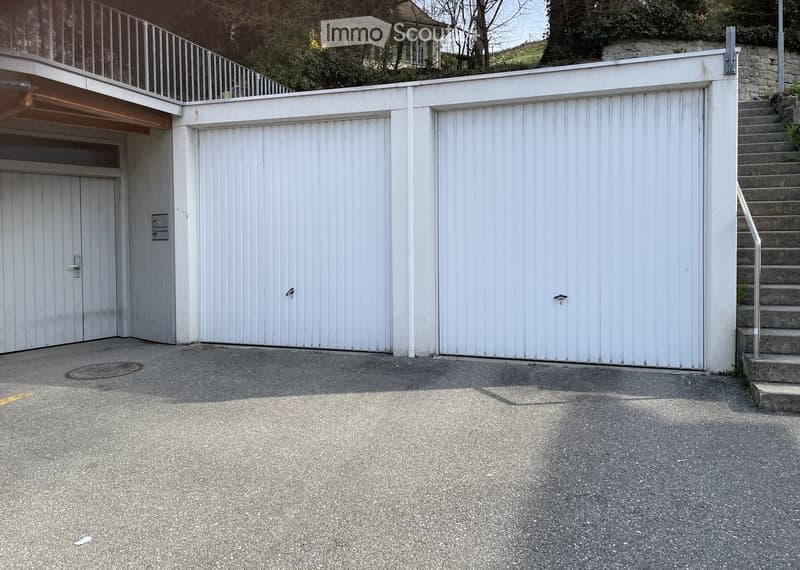 Closed garages, stairs leading to the upper floor, concrete parking lot