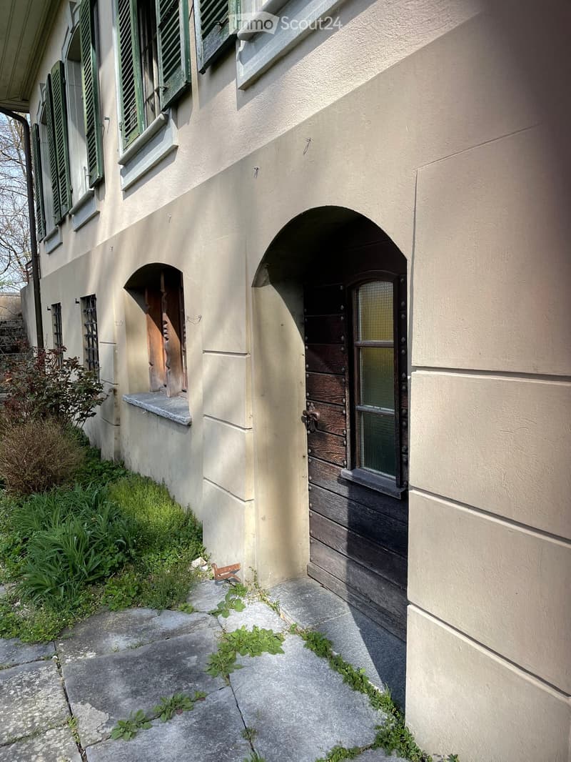old house, beige painted exterior, wooden windows, wooden door, paved walkway, greenery