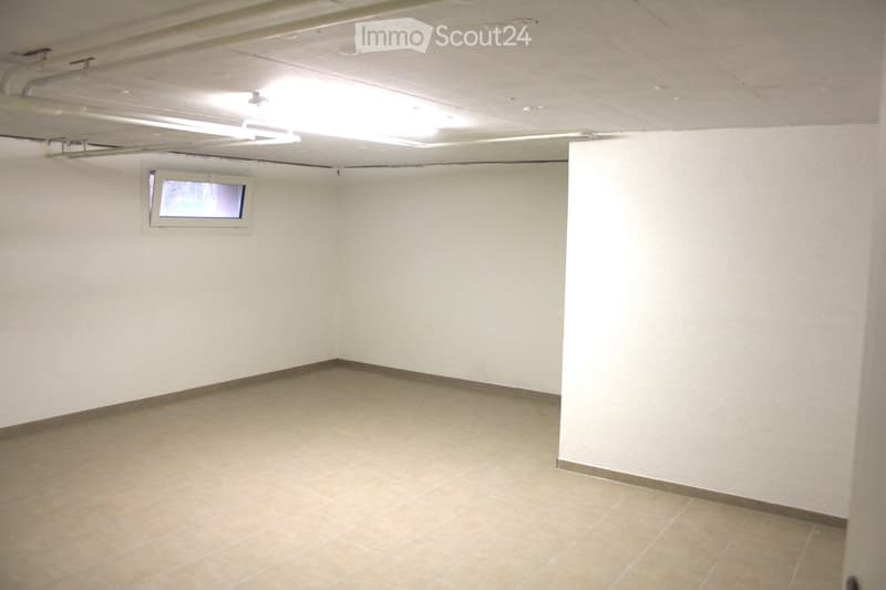 Empty room with white walls, tiled floor, small window, ceiling pipes, overhead light