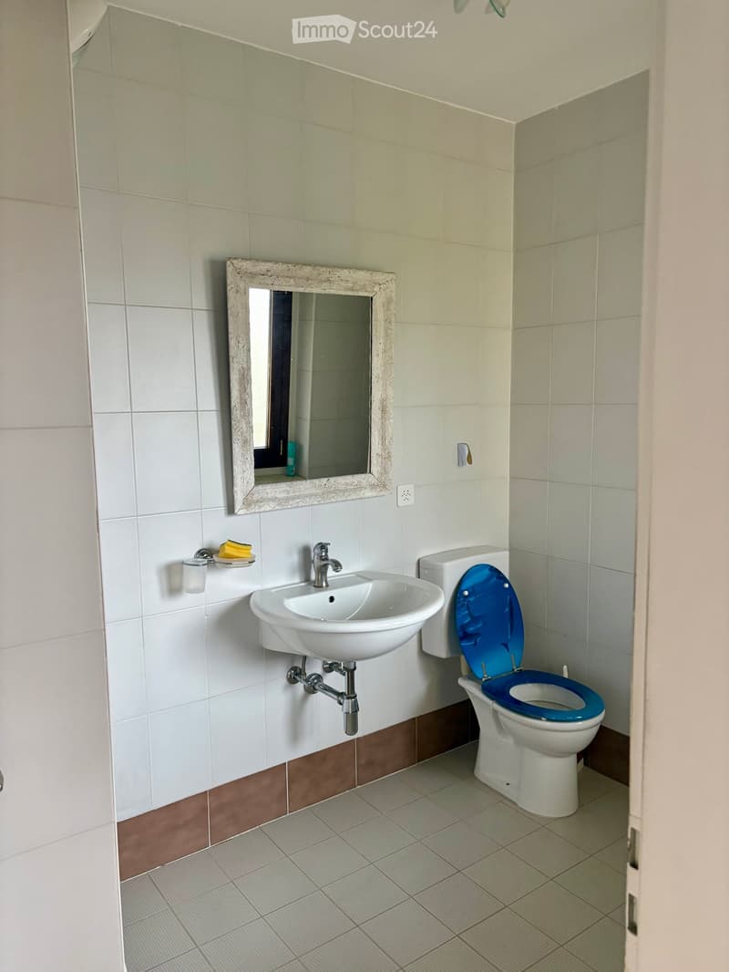 white tiled bathroom with sink, mirror, toilet, power outlet, and tiled floor