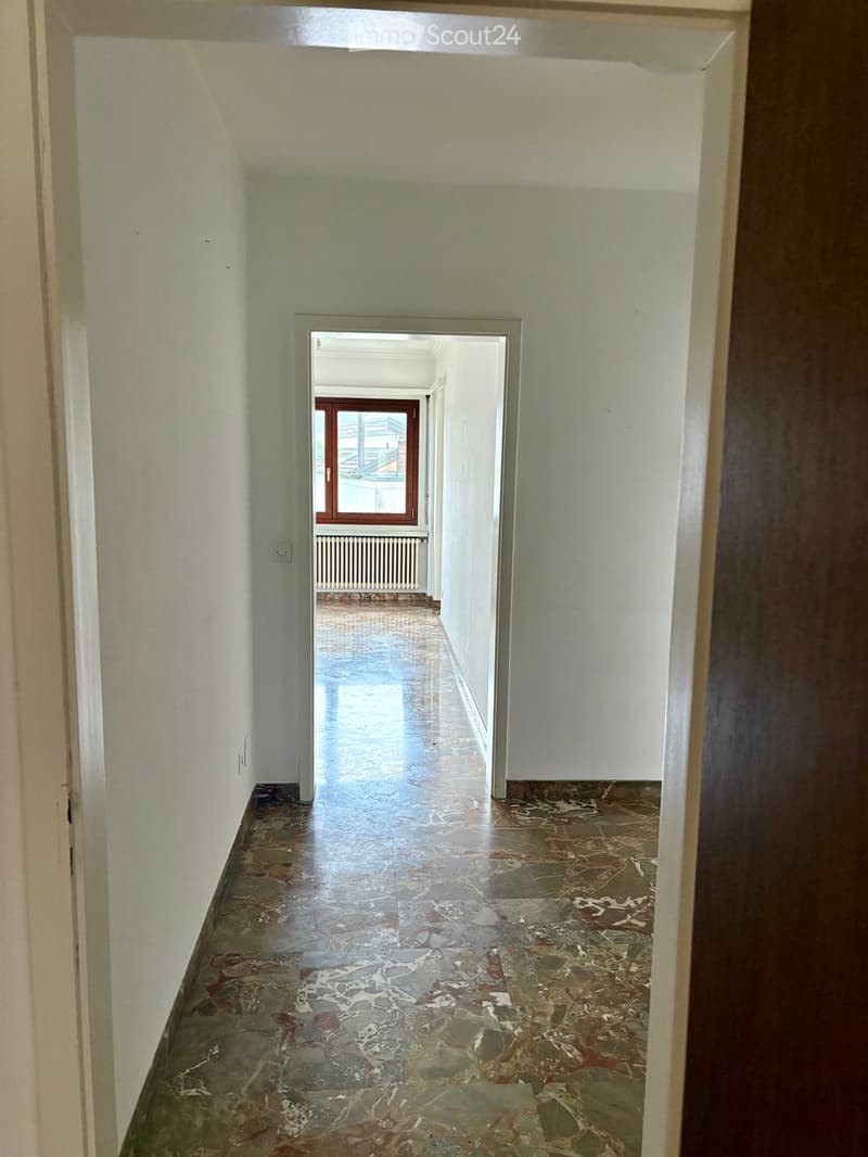 empty hallway with marbled flooring, windows with view on the outside, white walls, radiator
