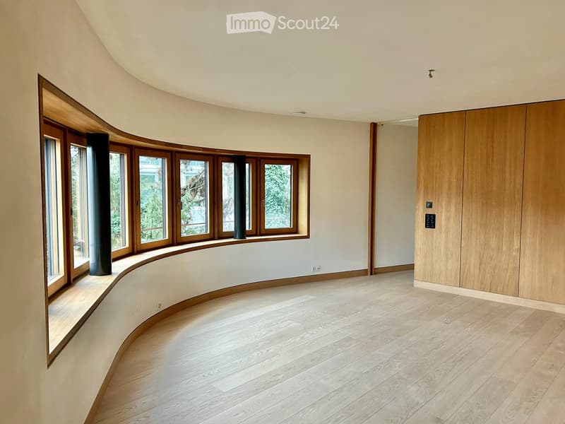 open room with curved walls, wooden floors, curved window seat, large windows, wooden cupboards