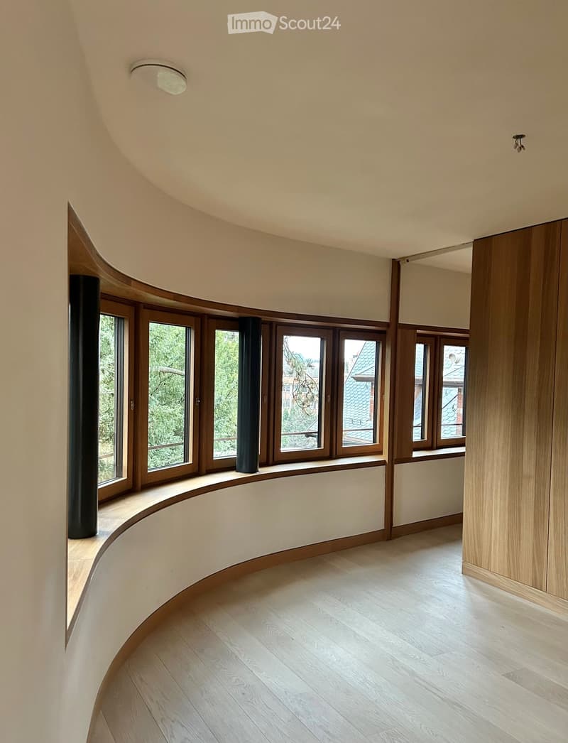 Room with wooden curved benches along large windows, wooden floor, light fixtures.