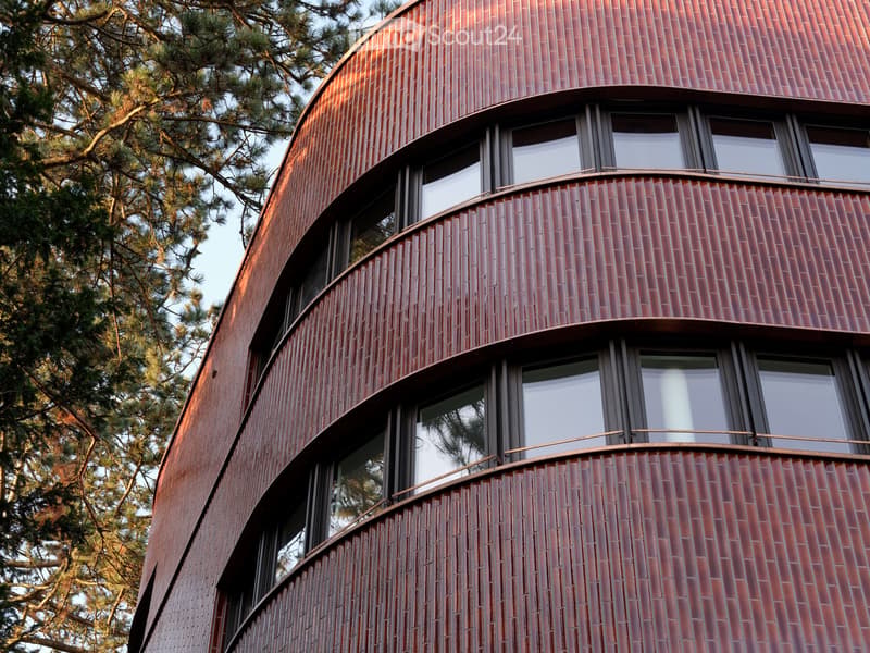 Modern building with red brick facade, large windows, and balconies.