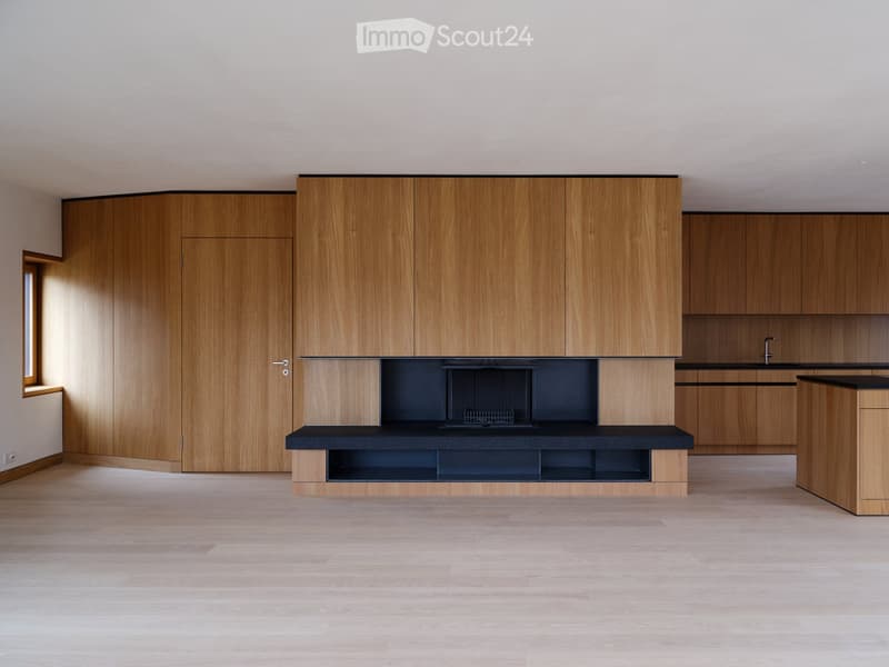 Modern kitchen with light wooden cabinets, black countertops, and a central island. The space is empty, with no appliances or furniture present.