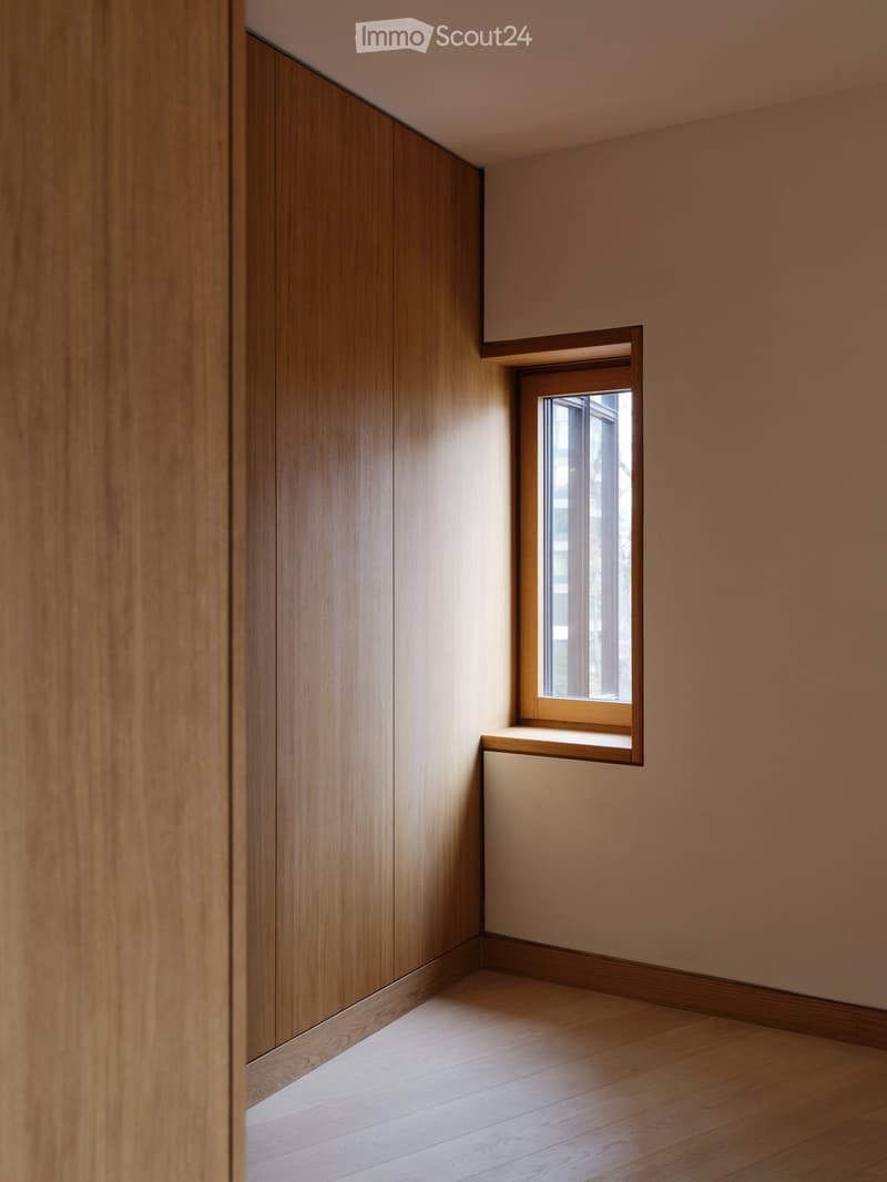 Empty room with wooden walls, light-colored wooden floor, and a small window letting in natural light.