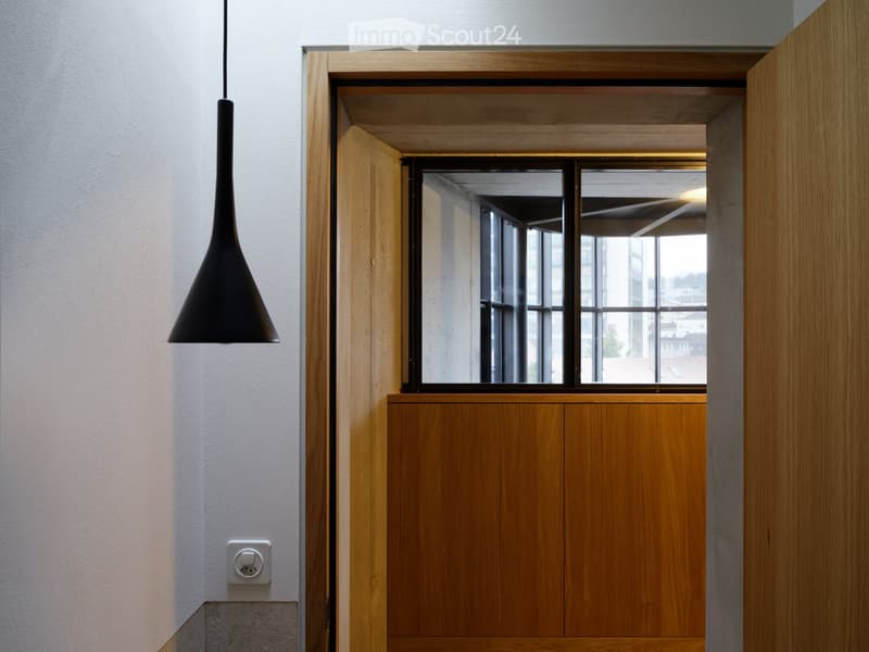Modern hallway with wooden door frame, pendant light fixture, and large window showing a view of the building exterior.