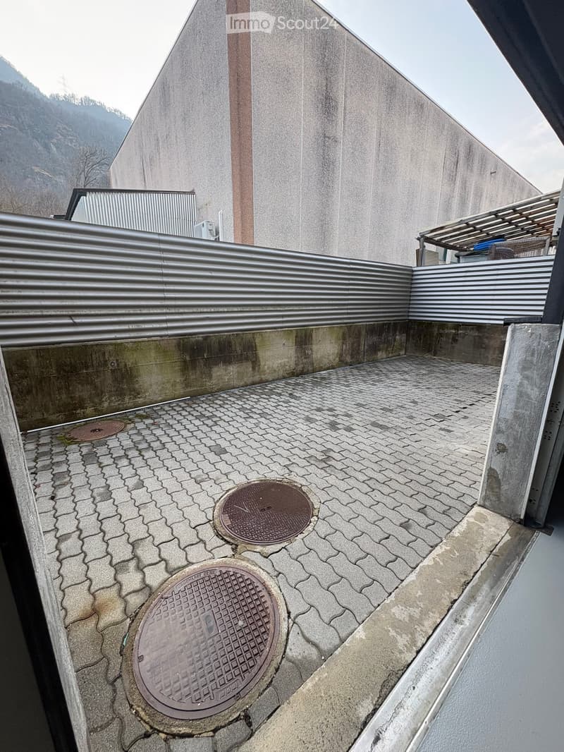 Exterior of a building with a brick wall, metal fence, and a paved area with two manhole covers.