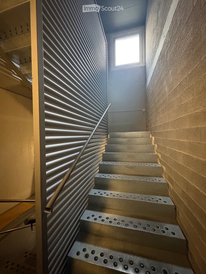Stainless steel staircase with a metal handrail, located in a building with a brick wall and a window
