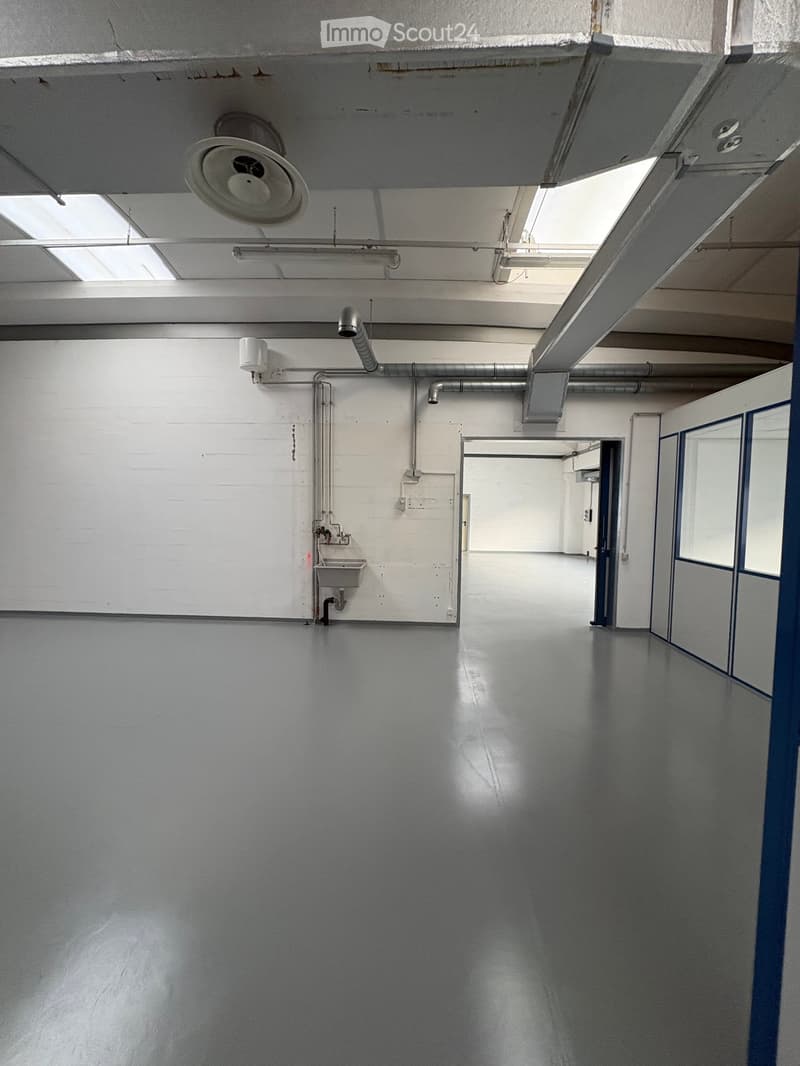 Empty room with white walls, gray floor, a sink, and pipes on the wall