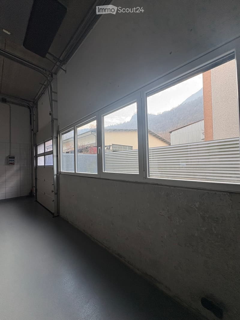 Empty garage with white walls, gray floor, large windows, and a door.