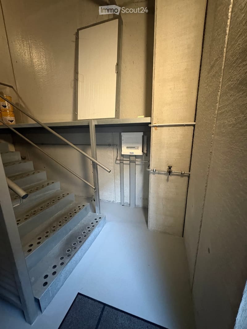 Concrete staircase with metal handrail, white painted walls, grey floor, utility box, pipes