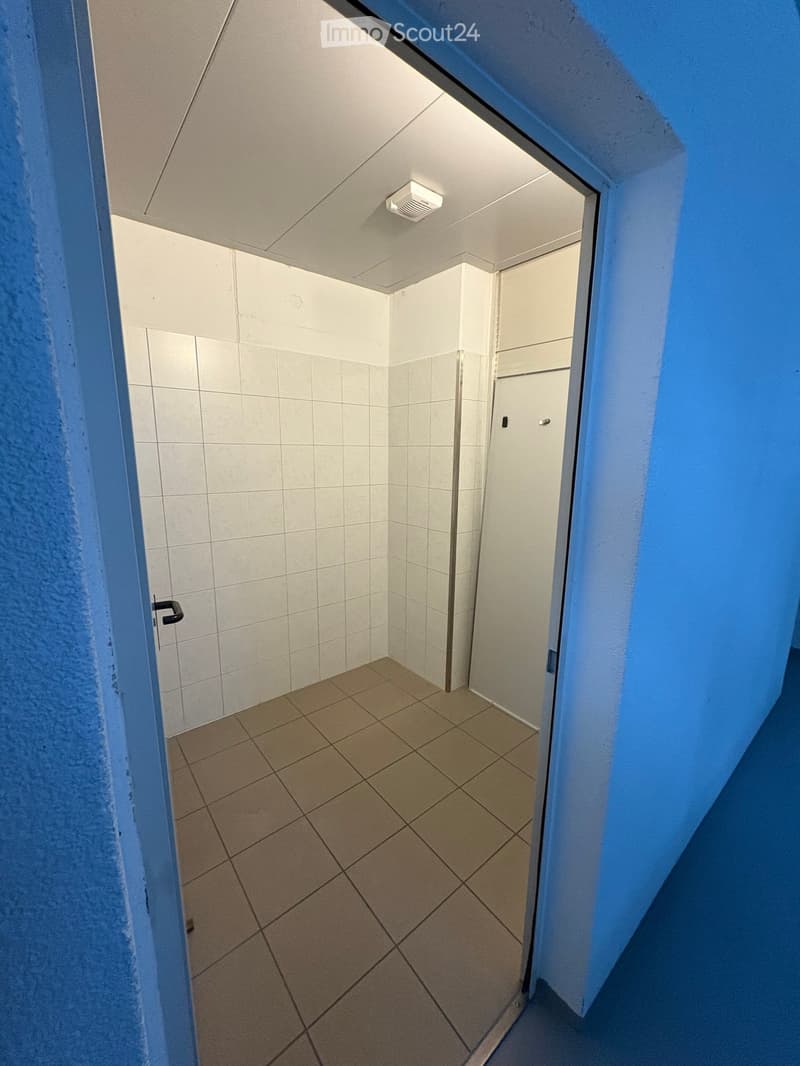 Empty room with tiled floor and walls, white ceiling, open door, and a white door on the right side.