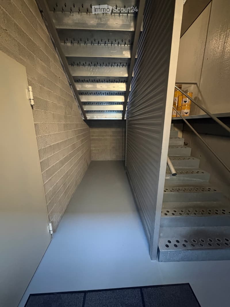 Concrete staircase with metal handrail, grey floor, brick wall, metal grates on the ceiling