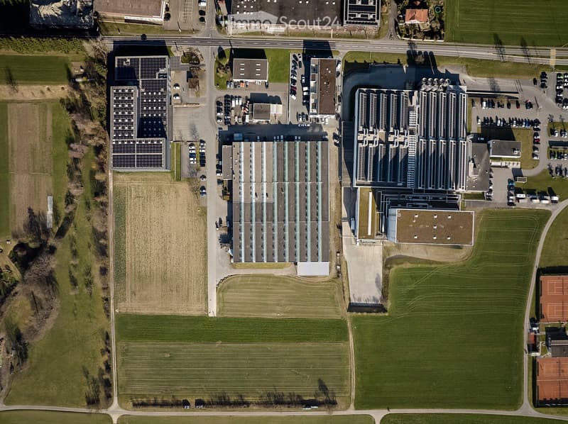 Industrial building with solar panels, multiple parking lots, surrounded by green fields